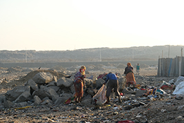 People collecting materials amidst a rocky landscape under a hazy sky, indicating a resource gathering activity, possibly in a low-income or informal setting.