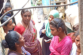 Women in traditional Indian attire engaged in a conversation in an urban environment, suggesting a community meeting or social gathering.